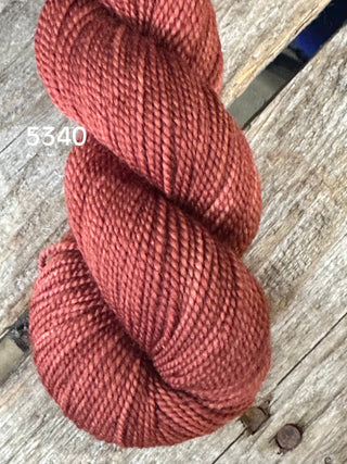 A close-up of a twisted skein from the KPM and KPPPM Variegated Color Collection in shade 5340, soft merino wool yarn resting on weathered wood—ideal for hand knitting projects.