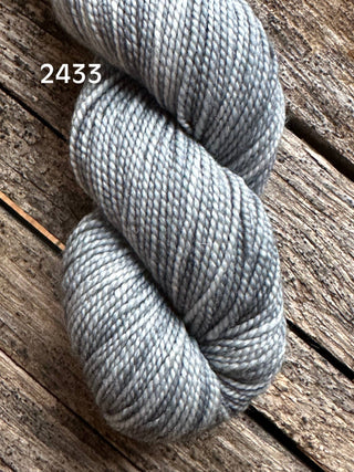 A skein of Koigu KPM & KPPPM Fingering Weight Yarn in light gray, subtly variegated, is displayed on a rustic wooden surface with the number 2433 shown in white text.