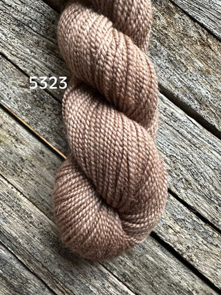 A skein of Koigu KPM & KPPPM Fingering Weight Yarn in soft, light brown (label 5323) is displayed on weathered wooden boards.