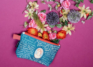 The Jane Austen Zipper Pouch, featuring a literary quote and portrait, rests on a magenta surface with bright flowers spilling from its opening—a vibrant arrangement perfect as a unique crafting project bag.
