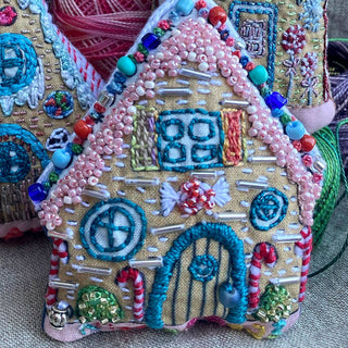 The Gingerbread Houses Embroidered Ornaments Sampler features a festive house-shaped ornament, detailed with holiday embroidery, colorful beads, sequins, windows, doors, and candy accents for a charming holiday décor piece.
