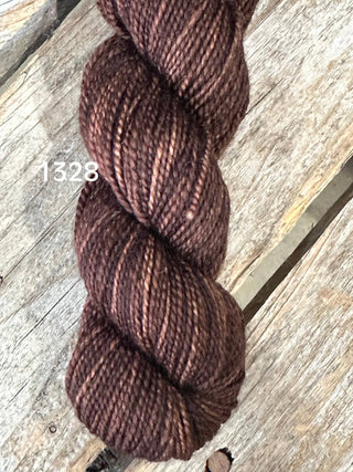 A skein of Koigu KPM & KPPPM Fingering Weight Yarn in brown with subtle lighter highlights, color 1328, rests on a weathered wooden surface.