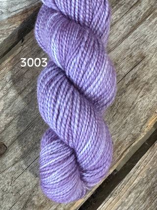 A skein of soft, shiny lavender yarn from the KPM and KPPPM Variegated Color Collection lies on a weathered wooden surface, perfect for hand knitting projects.