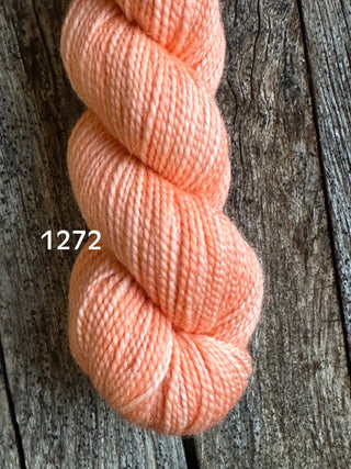 A skein from the KPM and KPPPM Variegated Color Collection in color 1272 rests on a rustic wooden surface, perfect for hand knitting with luxurious merino wool.
