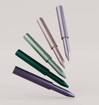 The Wren - Refillable Writing Pen set, featuring five metallic pens in green, teal, rose gold, silver, and dark purple with Japanese-made tips, is arranged diagonally on a plain light background with tips facing downward.