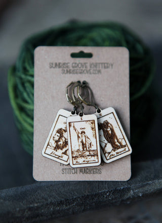 The Hermit, The Magician & Strength tarot card stitch markers are shown on a Sunrise Grove Pottery and Stitch Markers card in front of green yarn. Each wooden marker features an engraved tarot card design—perfect for knitting or as a progress keeper.