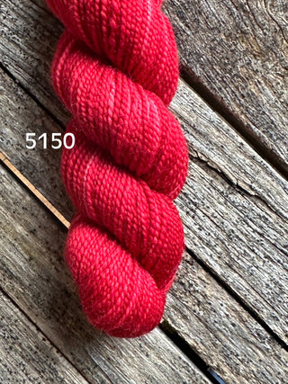 A skein of Koigu KPM and KPPPM Variegated Color Collection yarn in bright red 5150 rests on weathered wood, ideal for hand knitting projects.