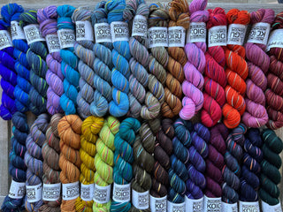 A vibrant array of KPM and KPPPM Variegated Color Collection Skeins is neatly arranged in rows, showcasing a wide range of shades. Each soft merino wool skein includes a white Koigu label, ideal for hand knitting projects.