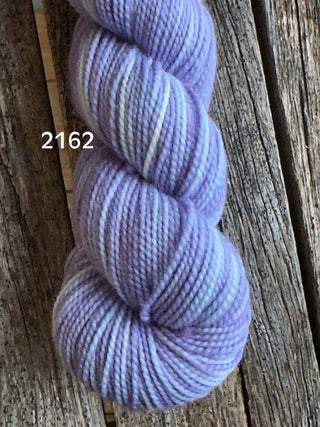 A skein from the KPM and KPPPM Variegated Color Collection in lavender and white (color 2162) sits on rustic wood—ideal for hand knitting cozy projects.