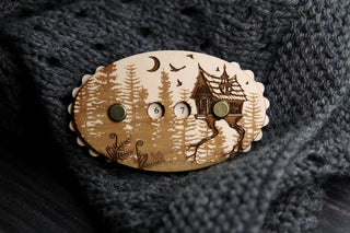 A beautiful wooden knitting row counter engraved with the Baba Yaga house in the forest, set on knit fabric.
