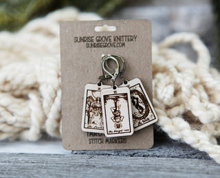 Three wooden Tarot Card Stitch Markers—The Fool, Death & Temperance—with metal clasps are displayed on a Sunrise Grove Knittery card. Perfect as knitting progress keepers or crochet accessories; yarn appears blurred in the background.