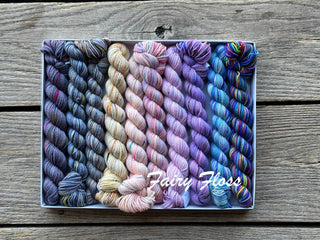 A Koigu Pencil Box in Fairy Floss—nine mini skeins of soft merino wool fingering yarn in gradient colors—displayed on a rustic wooden surface with Fairy Floss written across the bottom.