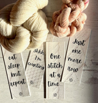 Four Printable Bookmarks for Knitters are displayed on a light surface with cream and pale pink yarn. Sunlight casts gentle shadows, highlighting the charm of these knitting-themed digital PDF bookmarks.