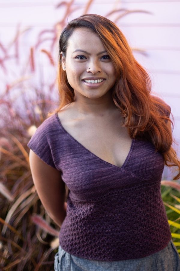 Light brown-skinned woman with flowing hair wearing a v-neck purple capped-sleeve knit sweater.