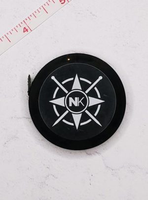 black Nomadic Knits tape measure against a white marble background