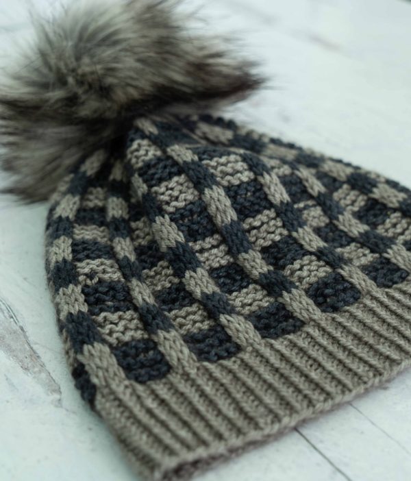 Higgins Lake hat, a grey and navy mosaic pattern with a floofy pom pom, knitting pattern by Jodi Brown of Grocery Girls knit, knit with AJHC indie yarn dyers yarn; found in Nomadic Knits creative knitting magazine
