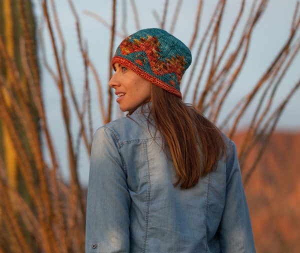 Brunette woman standing in front of a cactus wearing a blue denim shirt and fair isle knit hat; Kitt Peak Hat knitting pattern in Nomadic Knits creative knitting magazine Kitt Peak Hat knitting pattern in Nomadic Knits creative knitting magazine