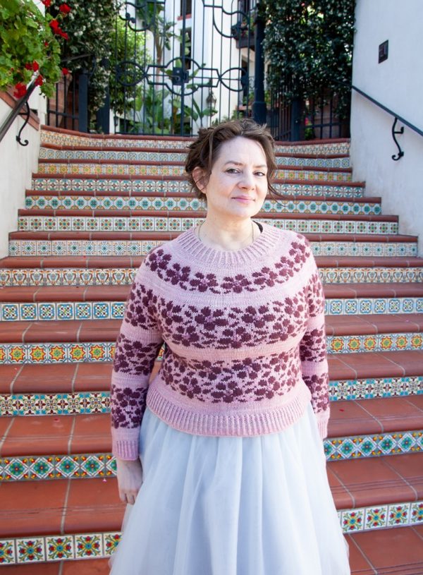 Mona Zillah modeling her Sakura sweater in front of brightly colored tile stairs. Sakura was knit using The Plucky Knitter indie dyed yarn; the pattern is available in Nomadic Knits creative knitting magazine