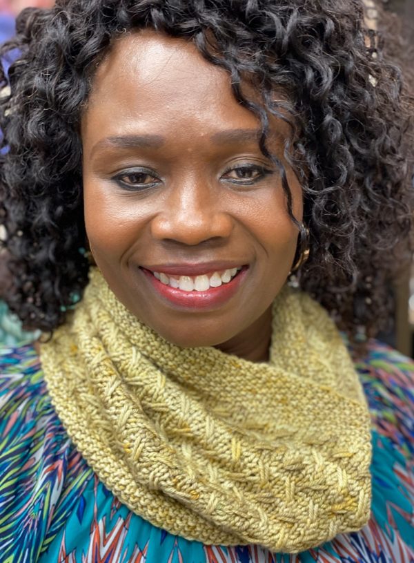 Beautiful dark skinned Black woman wearing a golden yellow knitted cowl; pattern in indie dyed yarn in creative knitting magazine